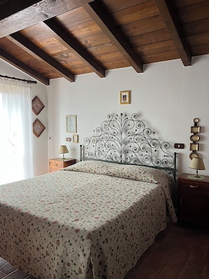 A bedroom with a bed, a nightstand, a lamp, and a decorative wall piece. - Cozy stone house surrounded by greenery (Emilia-Romagna)
