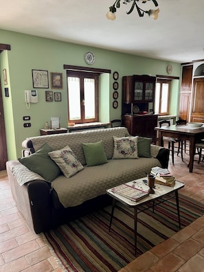 A living room with a sofa, a coffee table, and a dining area with a table and chairs. - Cozy stone house surrounded by greenery (Emilia-Romagna)