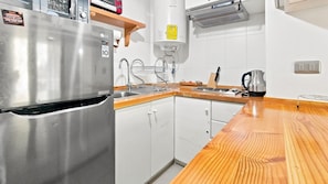 Una cocina con refrigerador de acero inoxidable, gabinetes blancos, encimera de madera, pileta y estufa.
