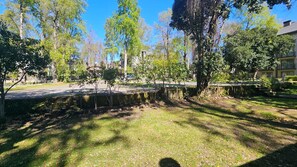 Un área con césped, árboles y un muro de piedra, un sendero pavimentado, y un edificio al fondo.