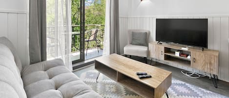 A modern living room with a sofa, a coffee table, a TV on a wooden stand, and a balcony with outdoor furniture.