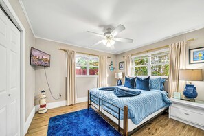 Een slaapkamer met een bed, een plafondventilator, een raam met gordijnen, een nachtkastje en een lamp.