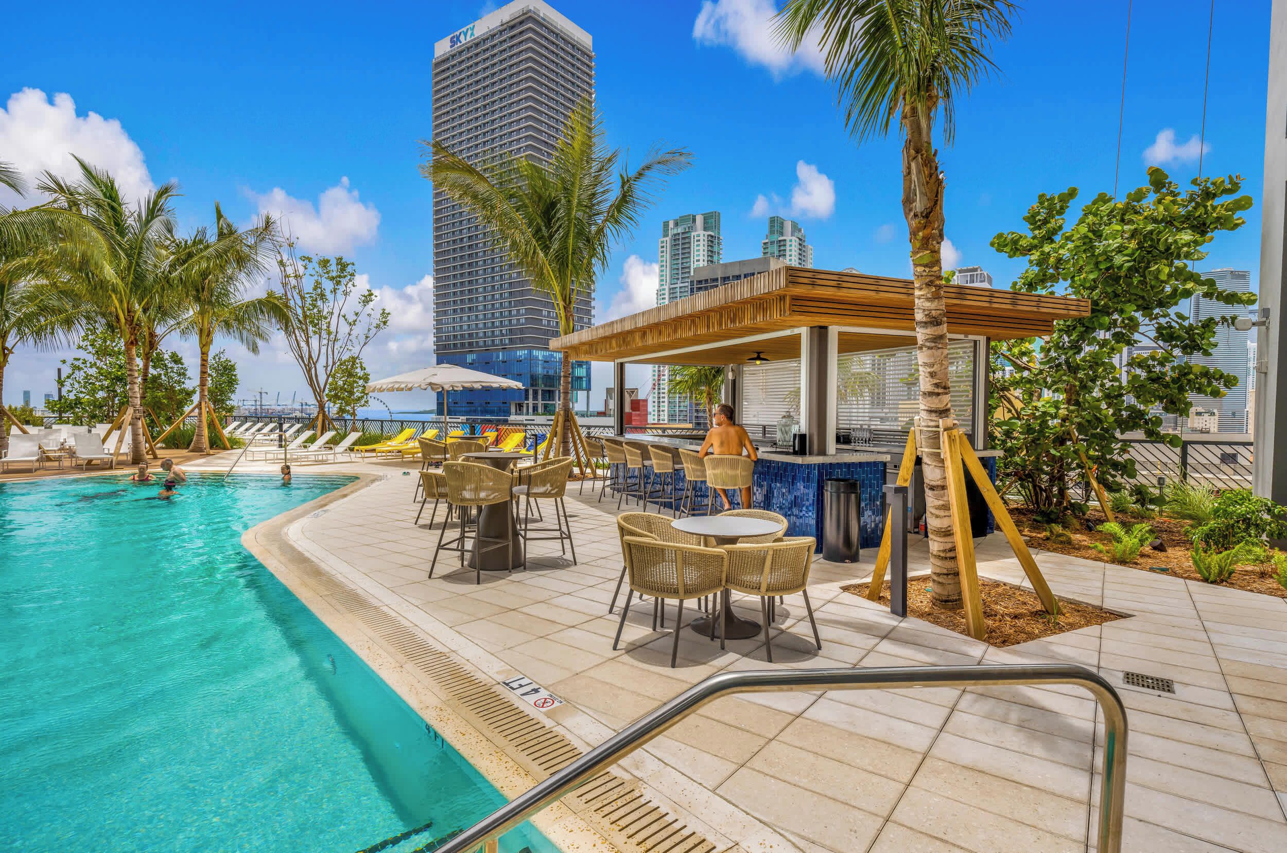 Ein Poolbereich mit Bar, Liegestühlen und Blick auf ein hohes Gebäude.