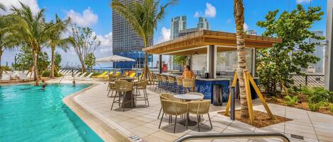 A poolside area with a bar, lounge chairs, and a view of a tall building.