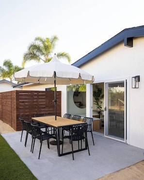 An outdoor patio with a wooden table and chairs, a white umbrella, and a brick wall. - The Horizon by Coastline Vacation Rentals (San Diego)