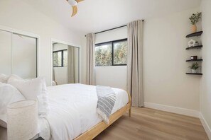 A bedroom with a bed, a window with curtains, a ceiling fan, and a wall-mounted shelf with plants. - The Horizon by Coastline Vacation Rentals (San Diego)