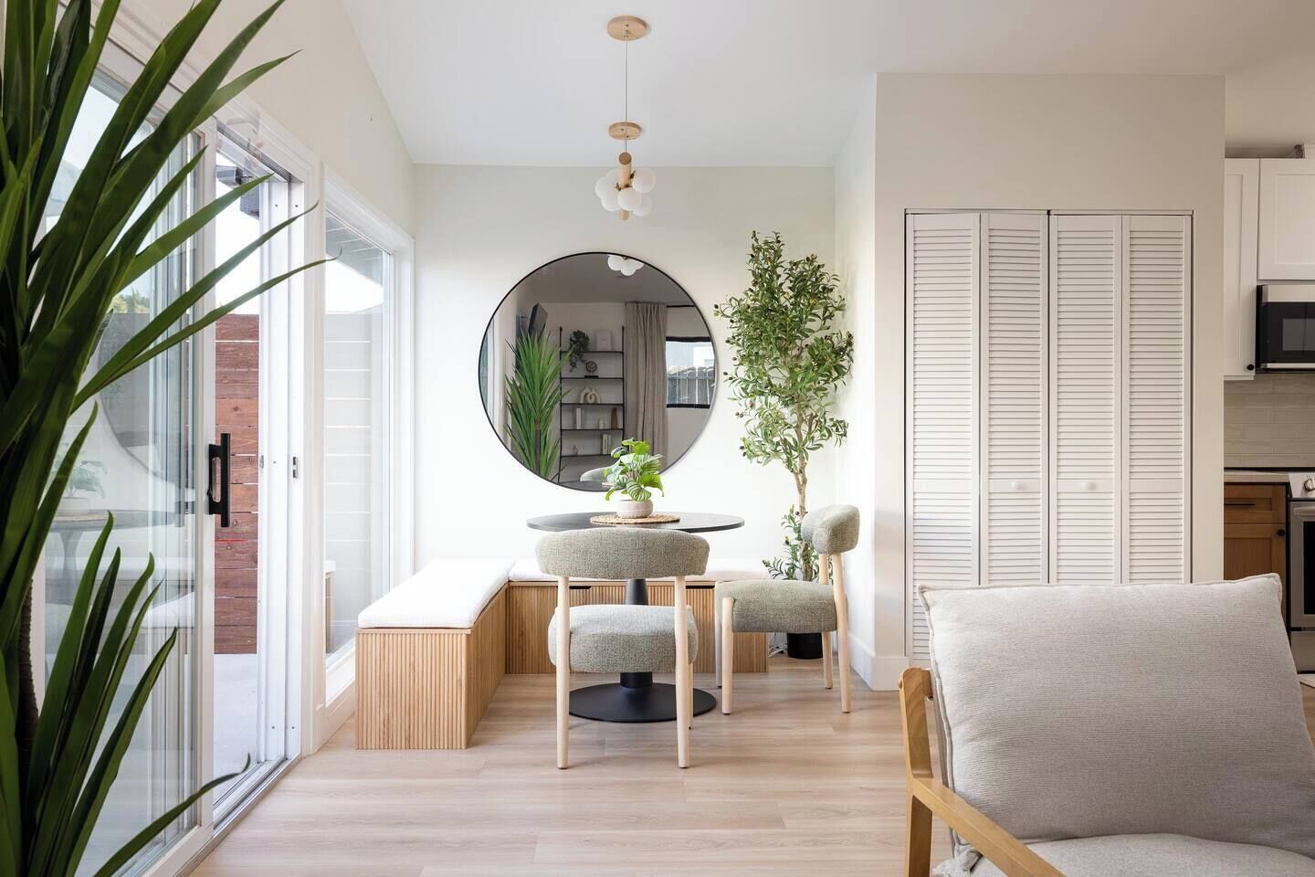 A modern living space with a round mirror, a dining table with chairs, a sofa, and a potted plant.