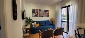 A living room with a blue sofa, two chairs, a TV, and abstract wall art. - JK & Faria Lima | Functional Apartment in Itaim Bibi (São Paulo)