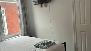 A bedroom with a bed, a flat-screen TV mounted on the wall, a window with curtains, and a door.