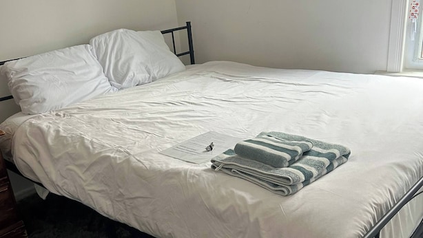 A bed with white bedding, a dark metal frame, and a grey and white striped blanket.