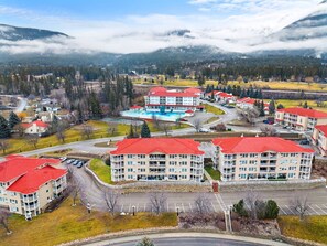 A multi-story hotel with red roofs, a swimming pool, and a mountainous backdrop. - Riviera | Balcony w/ Mountain Views | Pets | Golf (Fairmont Hot Springs)