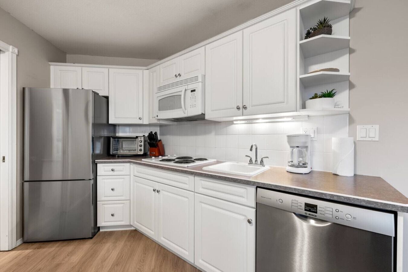 A modern kitchen with white cabinetry, stainless steel appliances, and a built-in dishwasher.