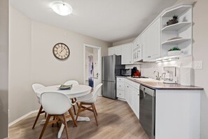 Una cocina moderna con armarios blancos, un refrigerador de acero inoxidable y un comedor con mesa y sillas blancas.