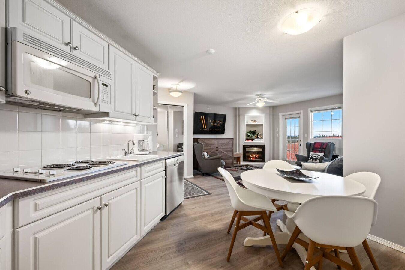 A modern kitchen with white cabinetry, a built-in microwave, and a dining area with a round table and chairs.