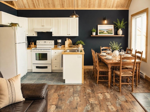 A modern kitchen with white cabinets, a built-in oven, and a dining area with wooden chairs and a table set for four.