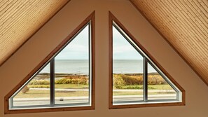 Una habitación con dos ventanas que dan al mar y a un paisaje con césped.