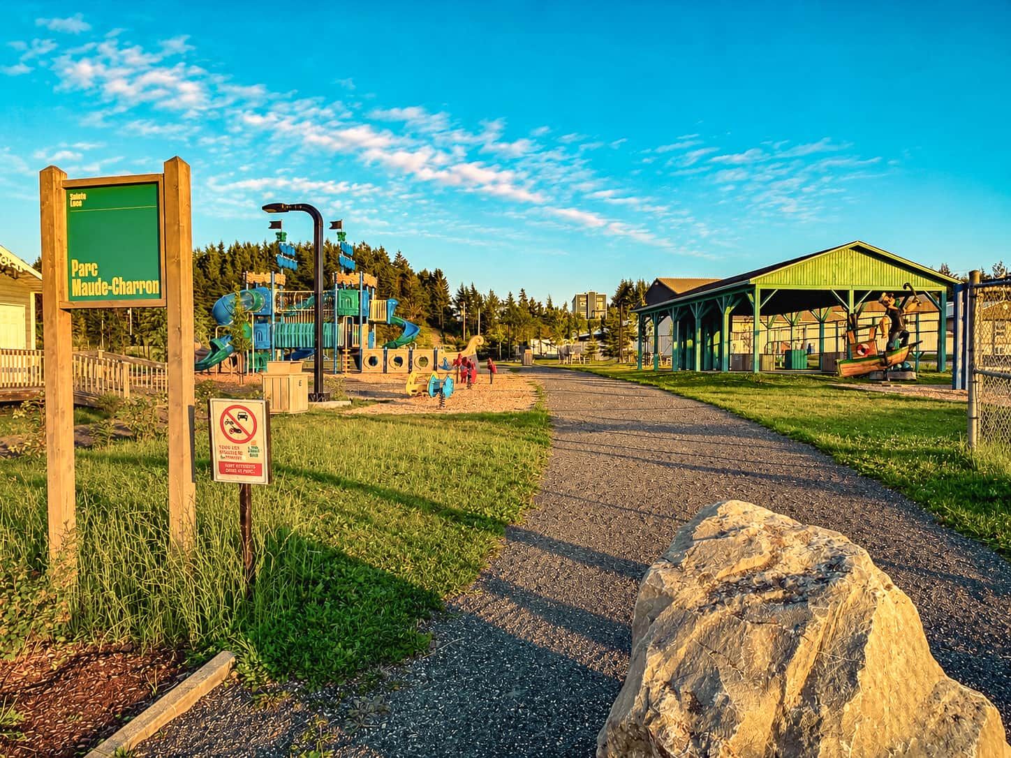 A playground with slides and climbing structures, a covered pavilion, and a sign indicating a parking area.