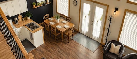 A modern interior with a dining area, kitchen, and seating space, featuring wooden floors, a view of the sea, and a staircase.