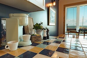 A kitchen with a coffee maker, a mug, a plant, and a window with blinds.