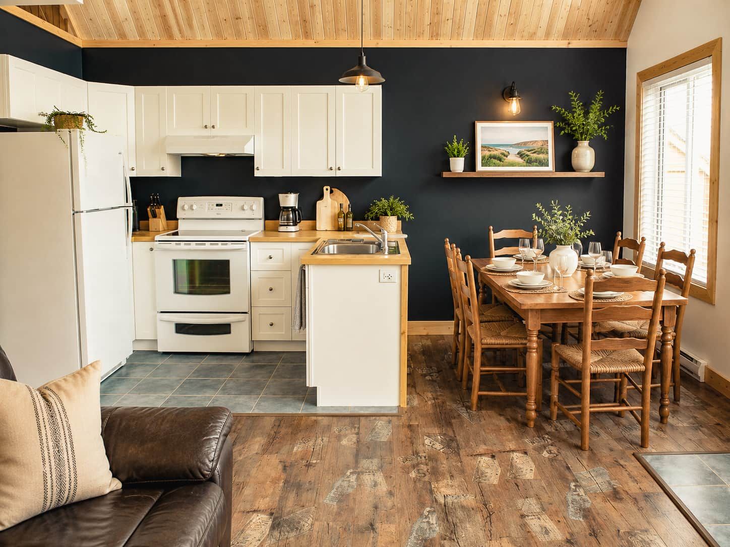 Una cocina moderna con armarios blancos, horno integrado y comedor con sillas de madera y mesa para dos.