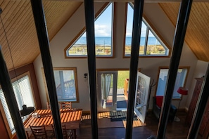 A multi-level interior with a view of the sea, wooden beams, and a dining area with a table and chairs.