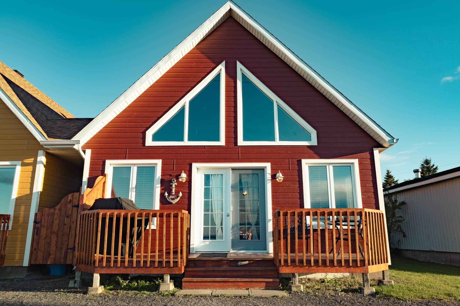 Ett tvåvåningshus med en röd fasad och vita detaljer, med en veranda framtill som har träräcken.
