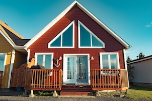 A two-story house with a red exterior and white trim, featuring a front porch with wooden railings.