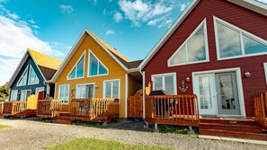 Una hilera de cabañas coloridas con terrazas de madera y ventanas amplias.