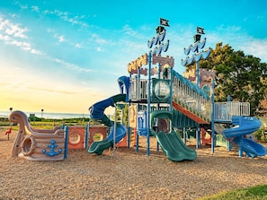 A playground with slides and climbing structures, set against a clear sky.