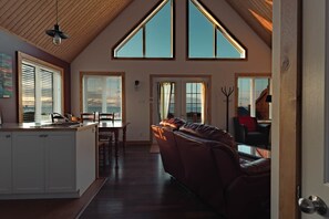 A spacious interior with a high ceiling, a dining area, a leather sofa, and a kitchen with a sink and cabinets.