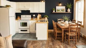 A modern kitchen with white cabinets, a built-in oven, and a dining area with wooden chairs and a table set for four.