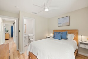 Un dormitorio con una cama, una mesita de noche, un ventilador de techo y un cuadro en la pared.