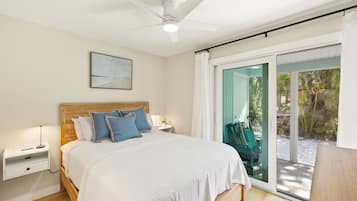 Een slaapkamer met een bed, nachtkastjes, een plafondventilator, een raam met uitzicht op palmbomen en een schuifdeur met glas.