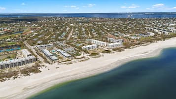 Vue aérienne d’un quartier résidentiel situé sur la côte, avec une plage, comprenant des maisons, des immeubles et une route.