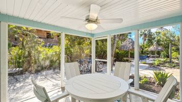 A covered patio with a round table and chairs, a ceiling fan, and a view of a tropical garden.