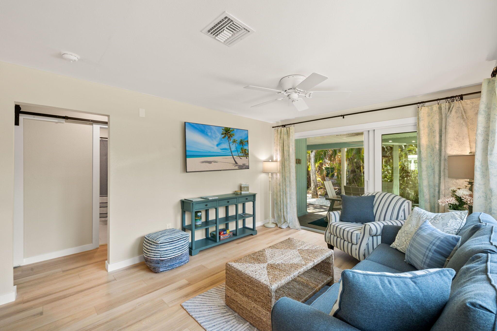 A living room with a sofa, ottoman, and a painting of a beach scene.
