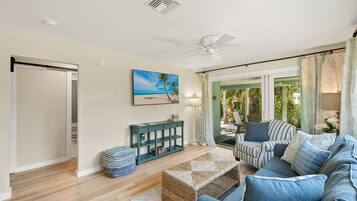 A living room with a sofa, ottoman, and a painting of a beach scene.
