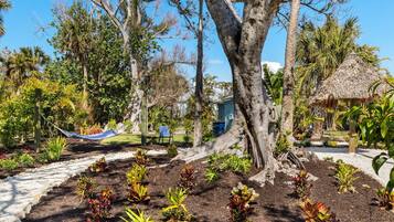 Un jardín con una hamaca, una estructura de techo de paja y diversas plantas.