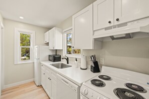 A modern kitchen with white cabinetry, a double sink, a microwave, a stove, and a window with a view of greenery.