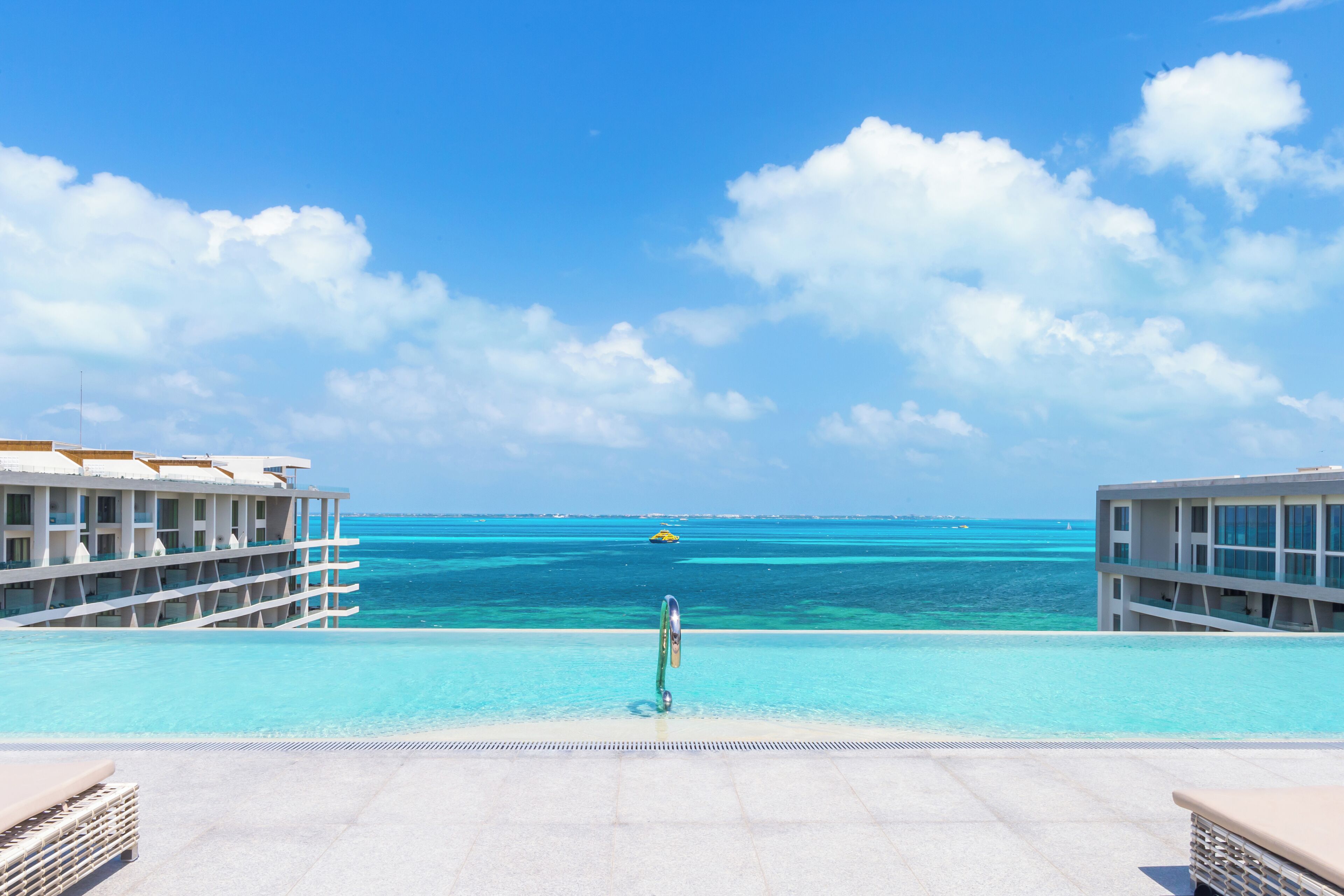 A poolside view with a clear blue sky, ocean, and a distant yellow boat.