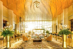 Eine großzügige Lobby mit einem gemusterten Teppich, einer zentralen Sitzecke mit Sofas und großen Fenstern, die natürliches Licht hereinlassen.