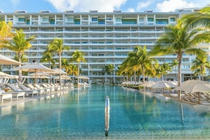 Ein Hotel mit einem großen Pool, umgeben von Palmen und Liegestühlen.