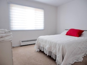 A bedroom with a bed, a window with blinds, a radiator, and a stack of folded towels. - Cozy Montreal Retreat - Shops - walk to everything (Montreal)