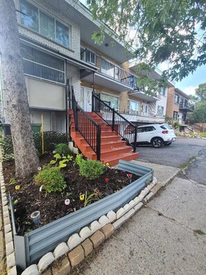 A residential building with a front entrance, a staircase, and a car parked on the street. - Cozy Montreal Retreat - Shops - walk to everything (Montreal)