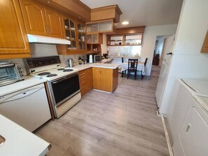 A kitchen with wooden cabinets, a stove, a microwave, and a dining area with a table and chairs. - Cozy Montreal Retreat - Shops - walk to everything (Montreal)