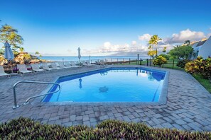 Ein rechteckiger Pool mit einer Metallleiter, umgeben von Liegestühlen und einer gepflasterten Terrasse.