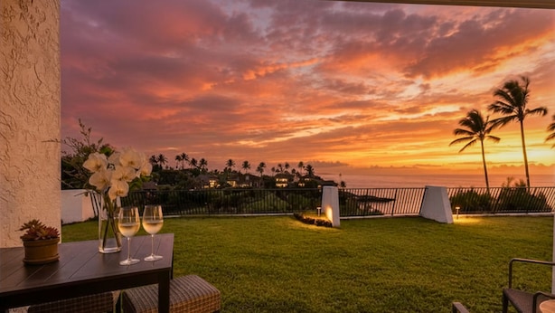 A patio with a view of a sunset over a coastal landscape, including palm trees and a fence. - Villa, Oceanfront, 1-bedroom (Napili-Honokowai)