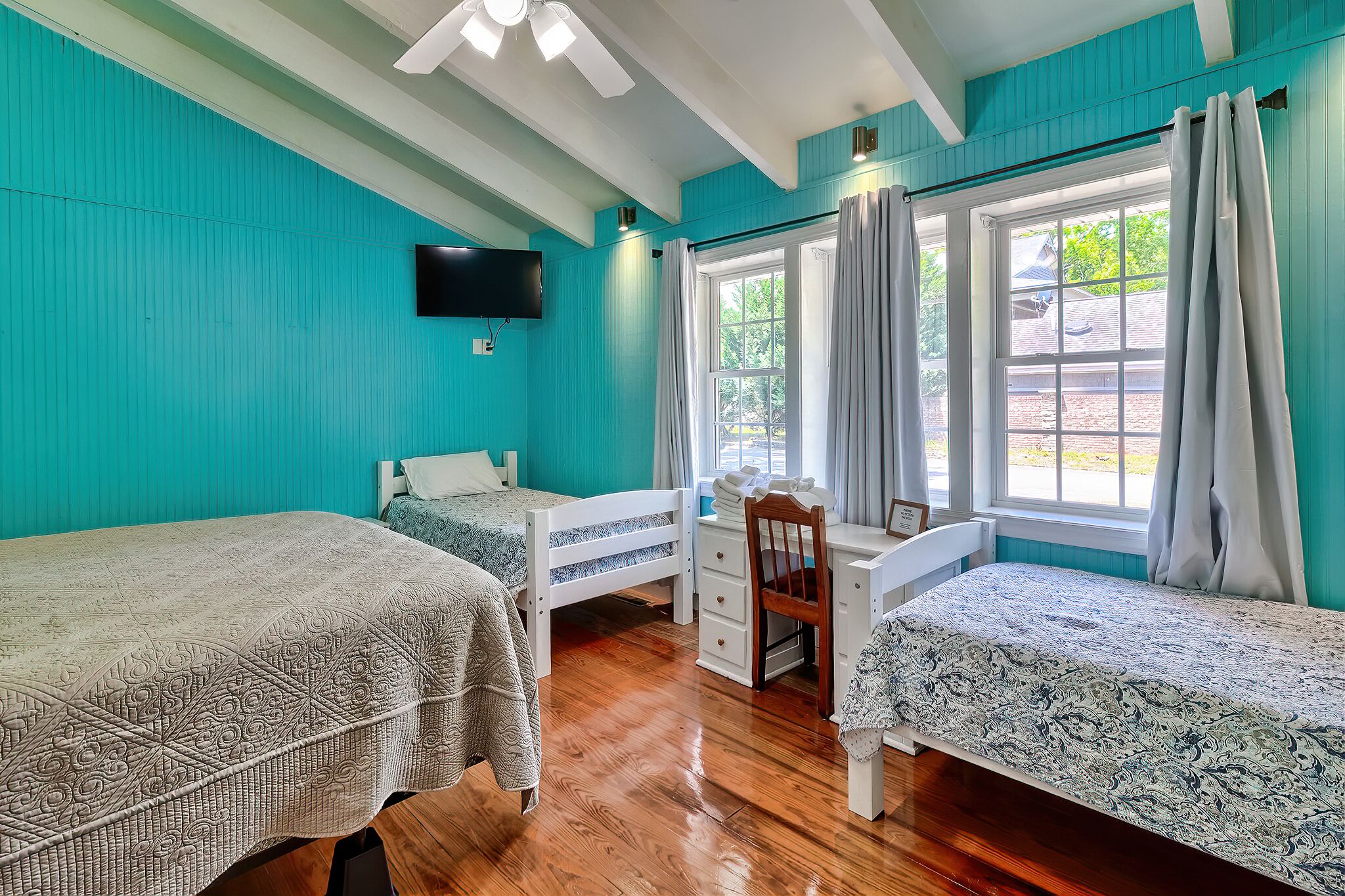 A room with two beds, a desk, a chair, a TV, and a window with curtains.