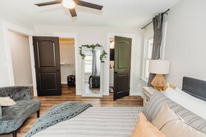 A bedroom with a bed, a grey sofa, a lamp, and a ceiling fan. - Close to FLW, 2 King Suites, Game Room, FirePit, Full Coffee Bar, Very Spacious (Waynesville)