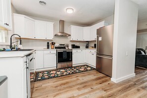 A modern kitchen with white cabinets, stainless steel appliances, and a wooden floor. - Close to FLW, 2 King Suites, Game Room, FirePit, Full Coffee Bar, Very Spacious (Waynesville)